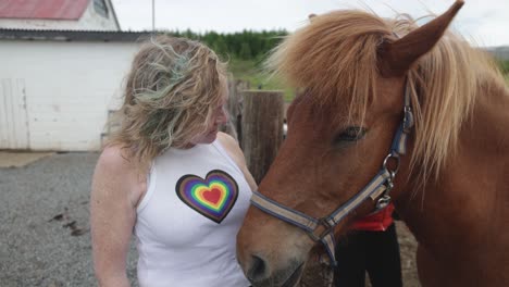 woman kissing and petting brown icelandic horse in iceland on ranch