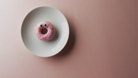 video of donut with icing on white plate over pink background