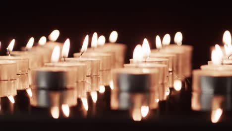 video of rows of tea candles with white flames and copy space on black background