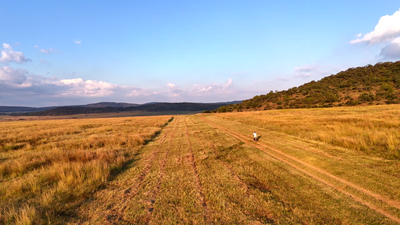 Girl cycles energetically along dirt road with mountains and blue sky behind