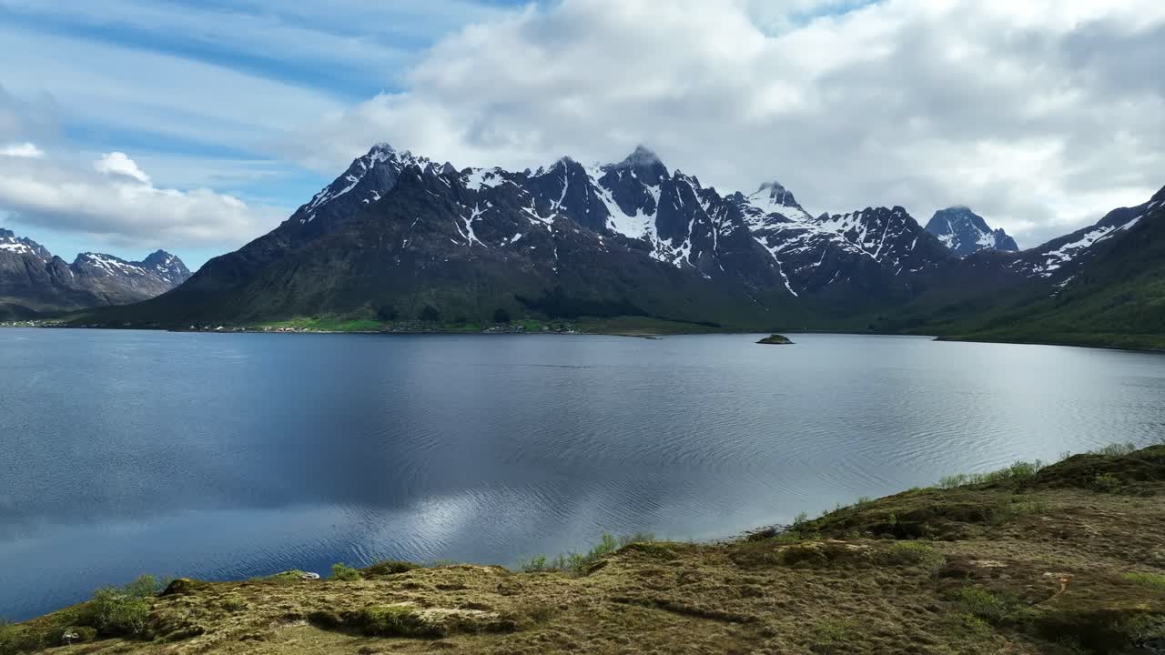 Græsenge og fjord ved Sildpollneset, der fører til skarpe Lofoten-tinder nær Laupstad, et stigende luftfoto fra foråret.