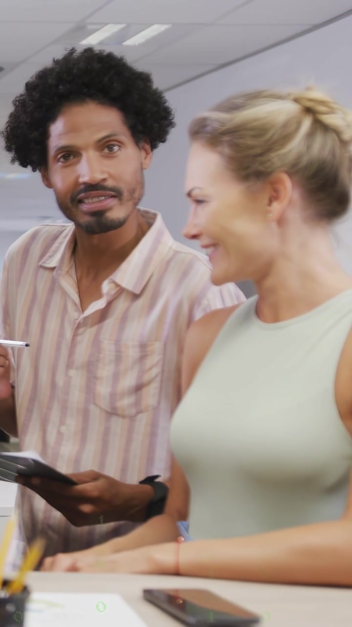 Vertical video: Man pointing tablet, woman tapping phone, making animated tech chart for biz review