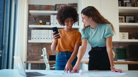 Zwei-Architektinnen-Mit-Laptop-Und-Mobiltelefon-Treffen-Sich-Und-Besprechen-Baupläne-In-Einem-Modernen-Büro