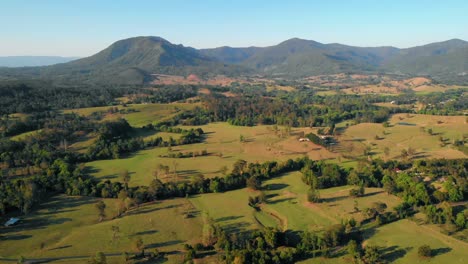 Vista-Aérea-De-Campos-Y-árboles,-Hacia-Las-Montañas,-Día-Soleado,-En-El-Campo-De-Nimbin,-Australia---Dolly,-Drone-Shot