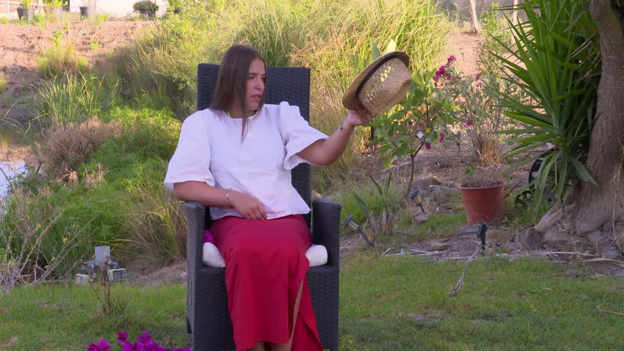 어린 소녀 가 정원 의자 에 앉아 태양 을 향해  모자를 들어 올리고 있다