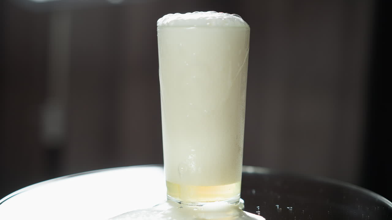 la espuma de cerveza pálida cae juguetonamente en cascada sobre la superficie reflectante y sombreada de una mesa moderna, sugiriendo un entorno íntimo para un momento refrescante.