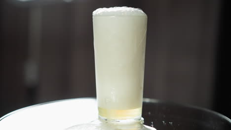 golden ale froths over the rim of a sleek glass, the pale beer foam playfully cascading onto the reflective, shadowed surface of a modern table, suggesting an intimate setting for a refreshing moment