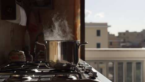 boiling cooking pan on heating stove on balcony background. gas flame heating pot and white steam rising from it on the background of solar glare. physical effects and abstract processes concept