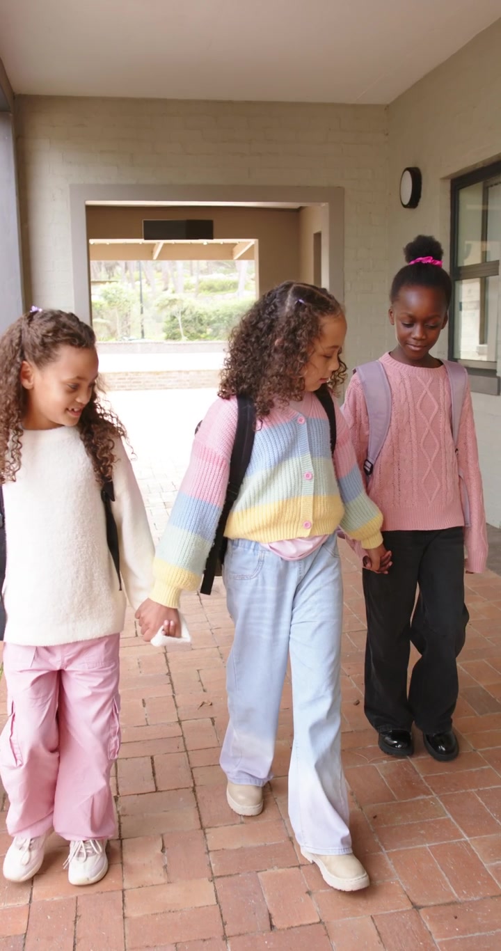 Vertical video: African American girls walking from arch down hall heading outside with backpacks
