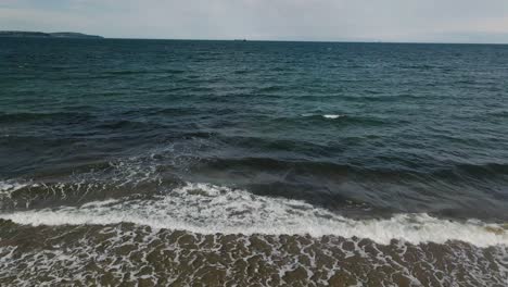 Aerial-view-of-waves-crashing-on-beach,-slow-motion