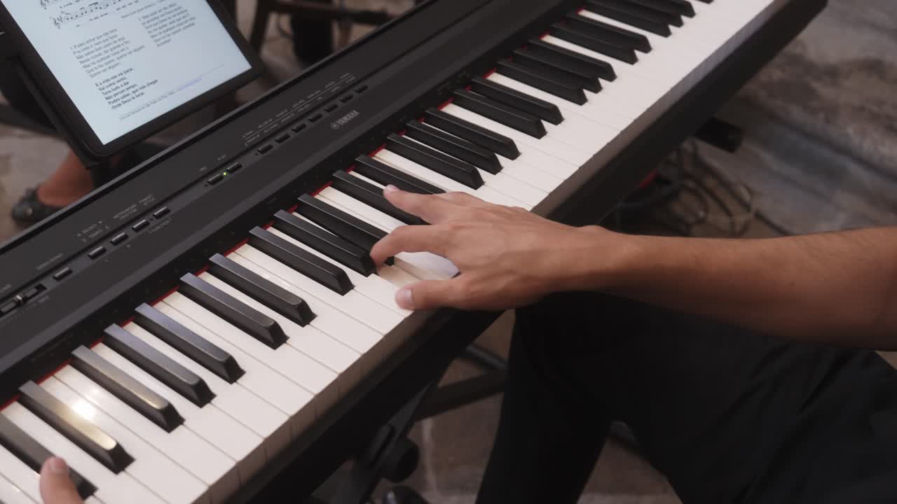 Hands playing piano keyboard with tablet displaying sheet music
