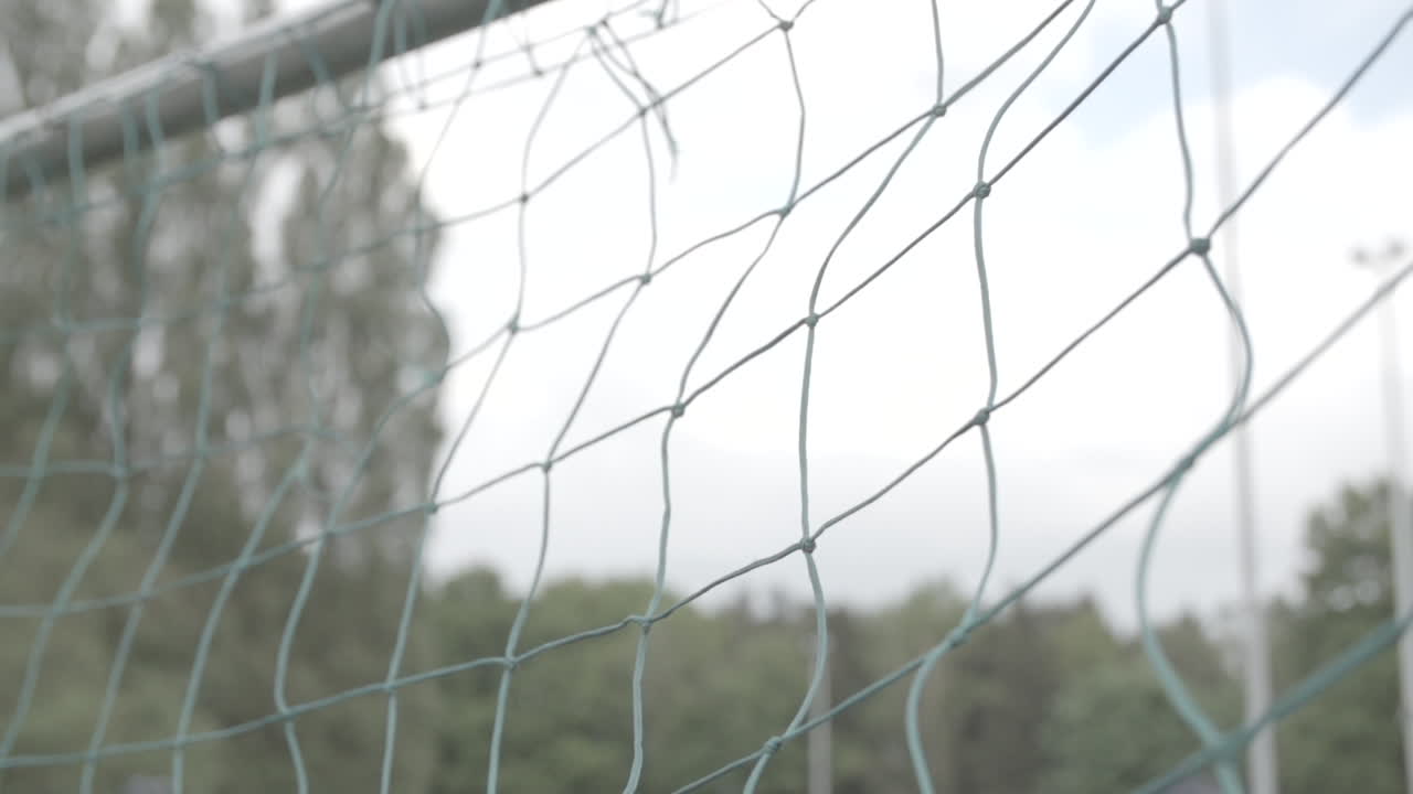 Close up slowmotion shot of a football flying into the green net of a goal on a cloudy day LOG