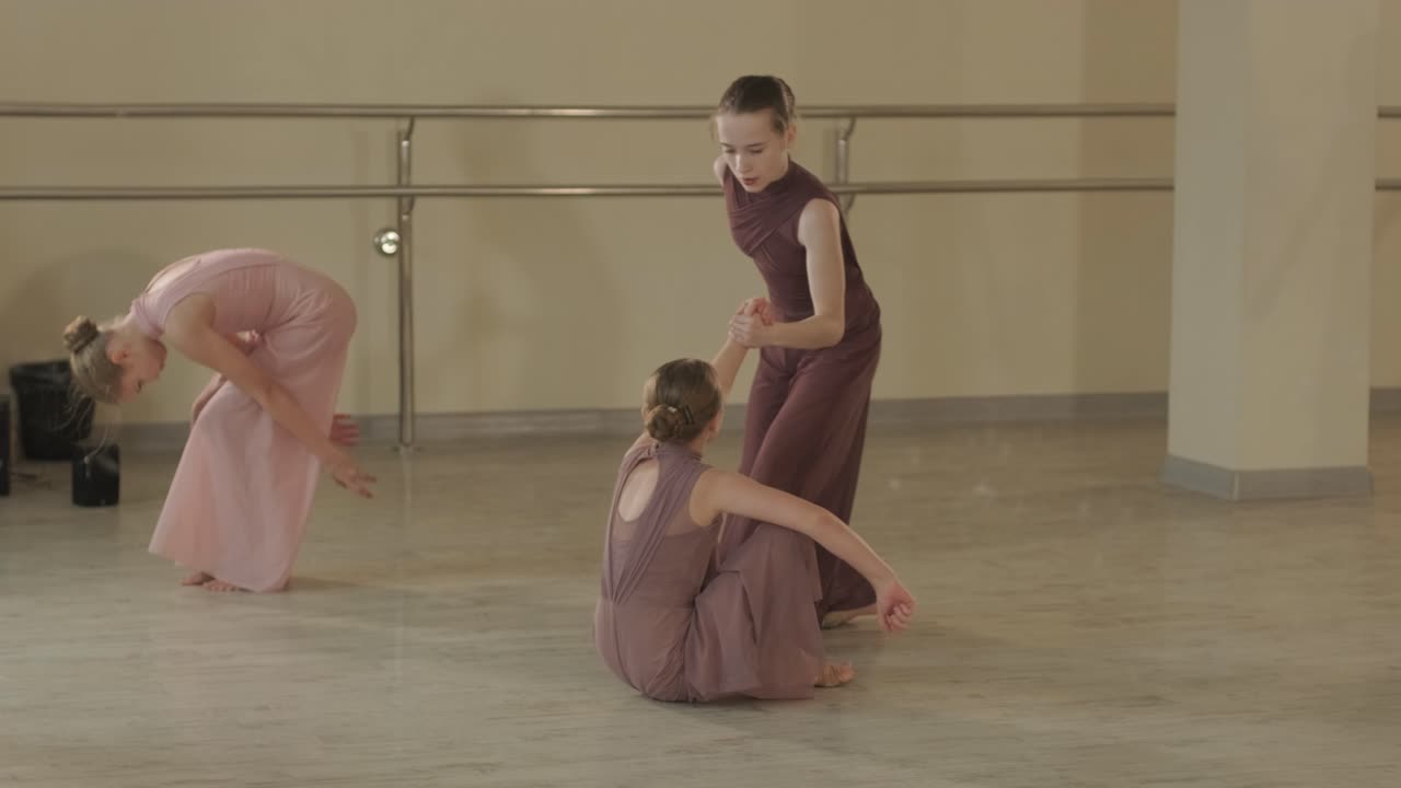 A group of young ballet students in black dancewear practicing positions in a spacious ballet studio with wooden flooring and wall-mounted barres. Focused expressions and synchronized movements.