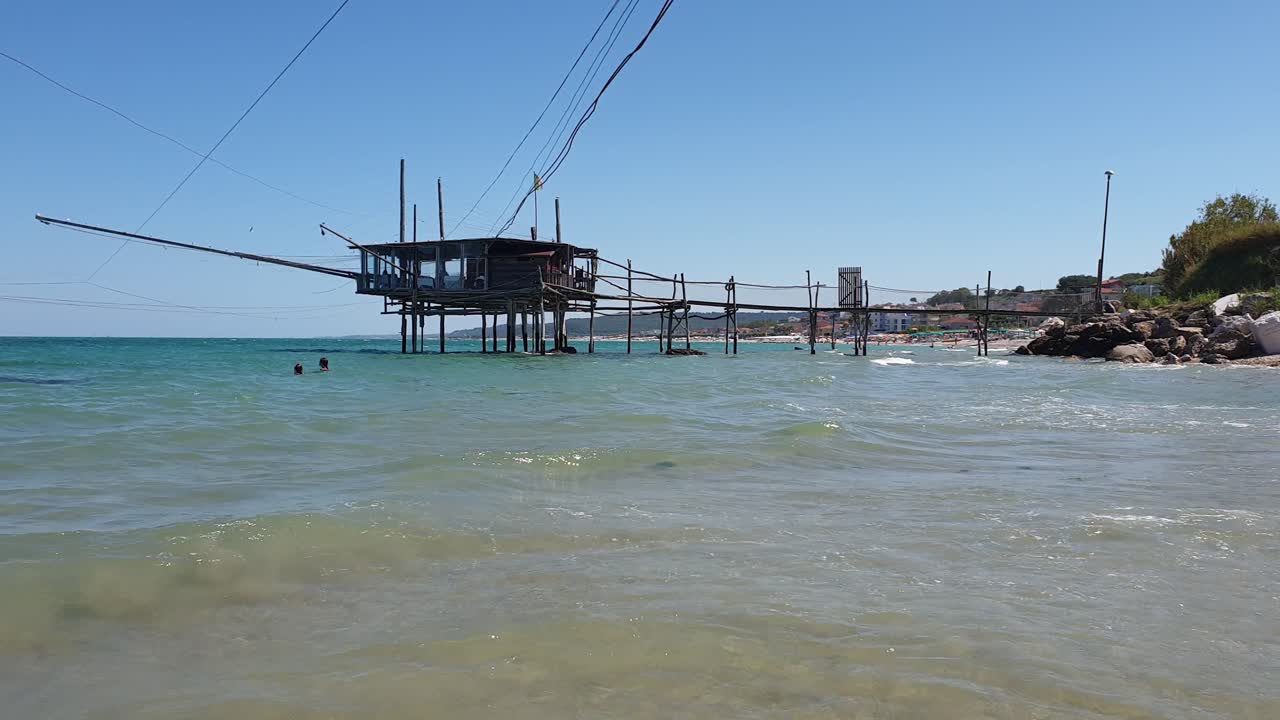 游客在costa dei trabocchi的海中游泳,背景是trabocco或trabucco