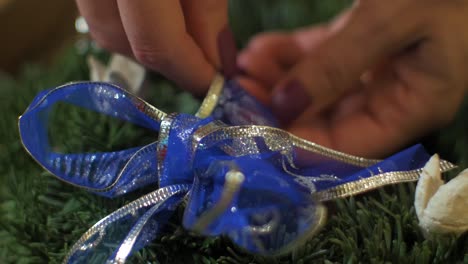 mujer haciendo una corona de adviento de abeto para la víspera de navidad y decorándola con cinta azul, decoración artesanal diy, tradiciones de invierno, vacaciones de temporada, manos de cerca