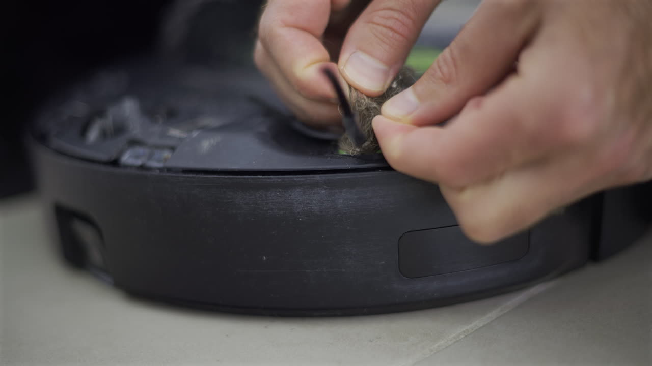 Close up of a man's hand cleaning the back of a robot vacuum cleaner