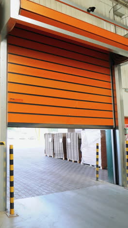 automatic roller gates of orange color are lowering down in the warehouse of woodworking plant. camera movement to the right. vertical video