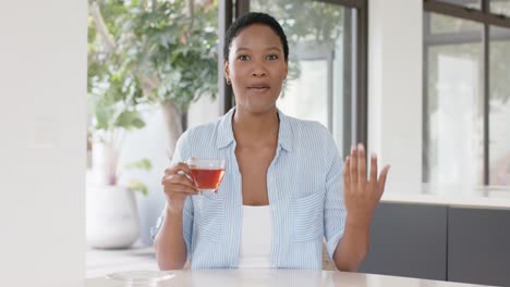 feliz mujer afroamericana sentada a la mesa, bebiendo té y haciendo una videollamada, cámara lenta