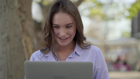 Mujer-Caucásica-Feliz-En-El-Parque-Enviando-Mensajes-De-Texto-En-La-Computadora-Portátil,-Riendo