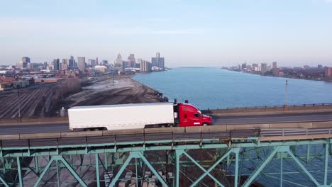 big rig semi truck and cars crossing at the ambassador bridge to canada, with detroit skyline in the background.-
