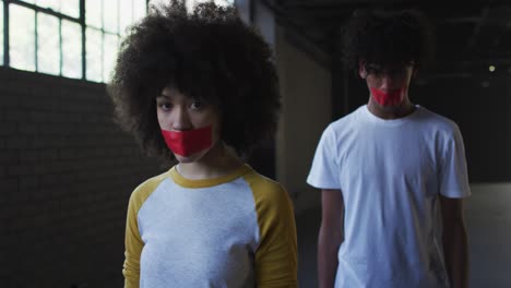 Portrait-of-african-american-man-and-woman-with-red-tape-on-their-mouth-in-empty-parking-garage