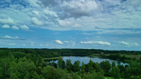 cinematic aerial shot flying over a forest and a lake with scenic clouds in the sky