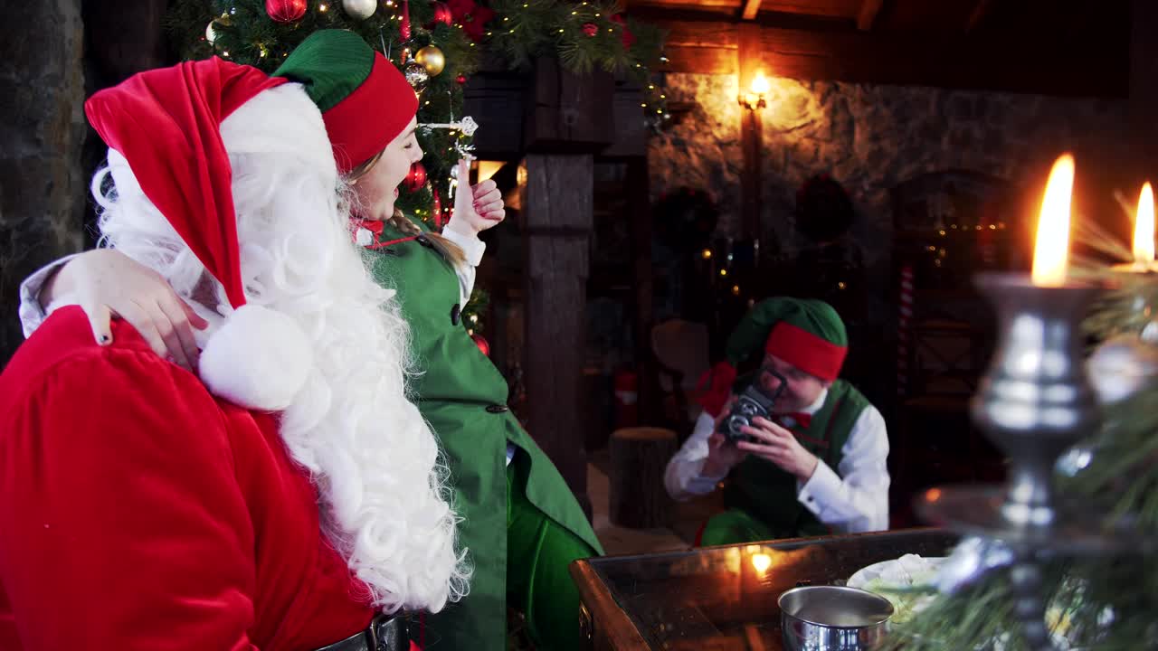 Fairy elves and Santa Claus at Christmas. Joyful friends elf and Santa with white beard making photos with retro camera