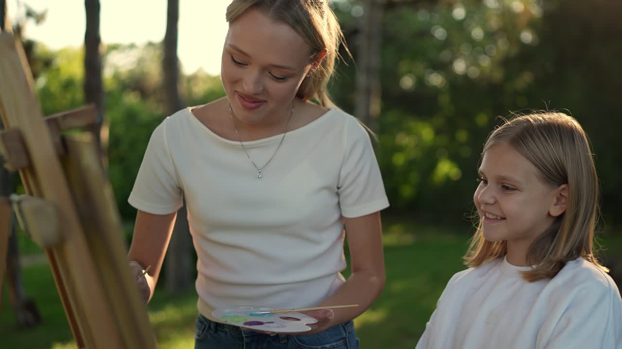 adolescente enseñando a una niña a pintar al aire libre