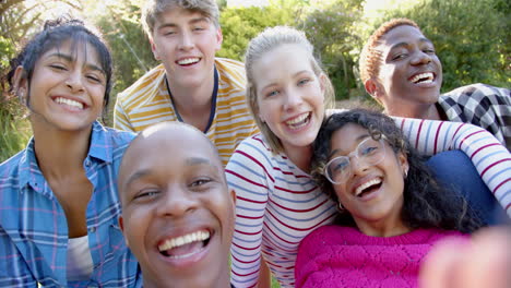 Happy-diverse-group-of-teenage-friends-sitting-on-grass-and-embracing-in-sunny-park,-slow-motion