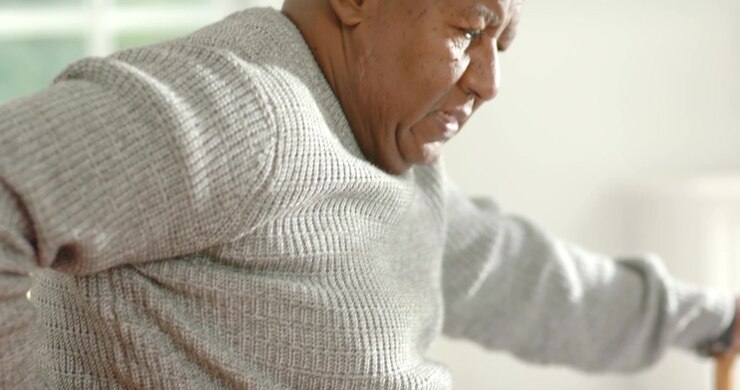 Senior African American man feeling sharp twinge, rubbing lower back on bed seeking relief