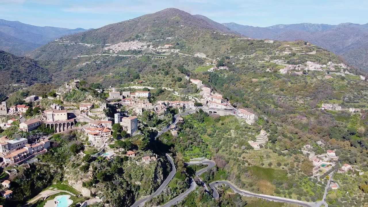 Villaggio collinare siciliano Savoca circondato da una lussureggiante valle mediterranea selvaggia e verde e montagne in una giornata di sole, Provincia di Messina, area escursionistica del Padrino, Sicilia. Ripresa drone rivelatrice.