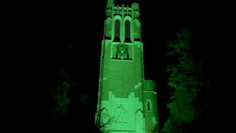 Beaumont-Tower-on-the-campus-of-Michigan-State-University-lit-up-at-night-in-green-in-honor-of-the-victims-of-the-February,-2023-mass-shooting-with-close-up-video-tilting-up