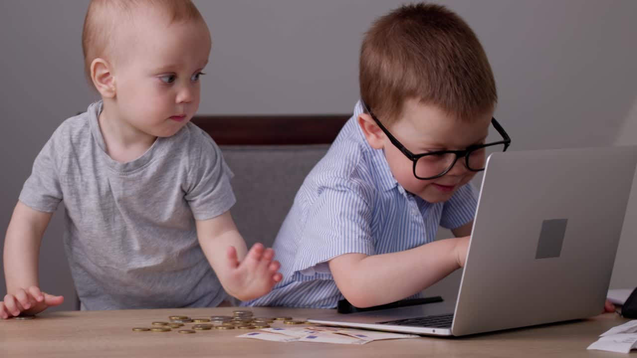 bebés caucásicos niños jugando con monedas de dinero, computadora portátil en la mesa de escritorio