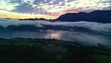 aerial view of ethereal sunset, drone panning above tarn, mountains silhouette depict vibrant skyline