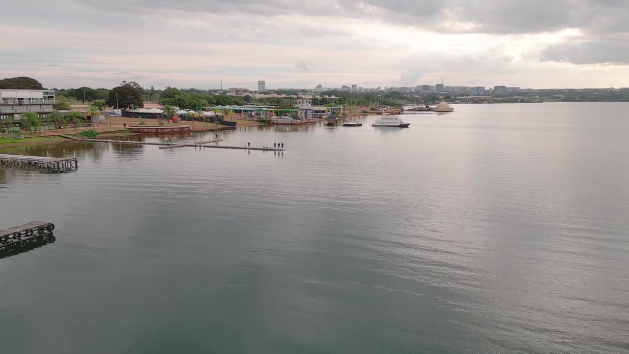 Lago Paranoá a Brasília, Distretto Federale, Brasile, vicino al quartiere Lago Sul, con acque calme del bacino idrico, strutture portuali e sviluppo urbano della costa, ripresa in planata in avanti con drone.