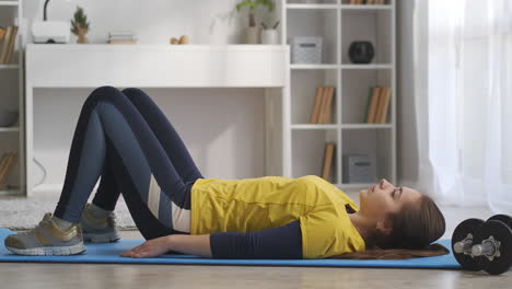 Una-Mujer-Joven-Está-Entrenando-En-Un-Apartamento-El-Fin-De-Semana-Tumbada-En-El-Suelo-Y-Haciendo-Ejercicios-Para-Los-Músculos-Abdominales-Para-Mantenerse-En-Forma-Y-Preocuparse-Por-Su-Buena-Condición-Física