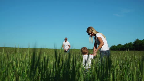 happy family: mother and son go to the field to his father who plays with a football