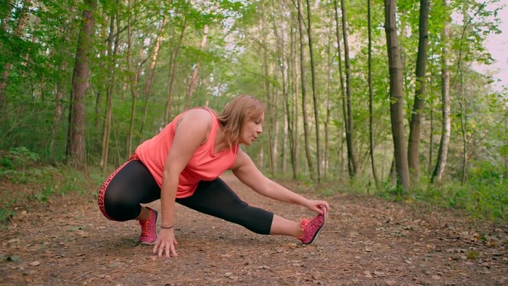 Caucasian women in sportswear stretching legs and exercising in the forest trail