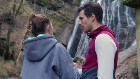 loving couple holding hands, talking while enjoying waterfall scenery, medium