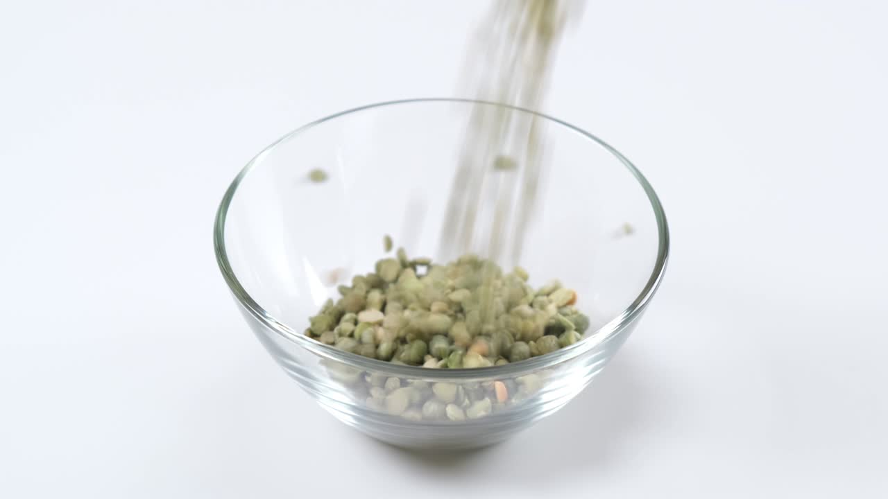 Dry green split peas falling into a glass bowl on white background