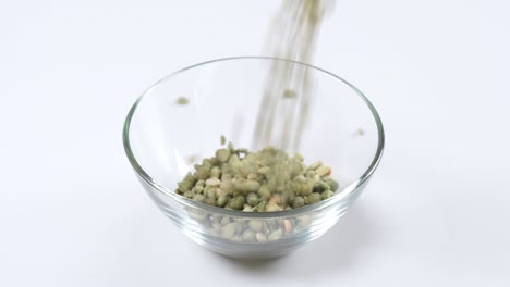 dry green split peas falling into a glass bowl on white background