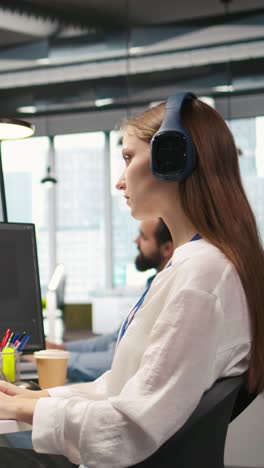 Vertical video Young female programmer in office reviewing AI system metrics, listening music