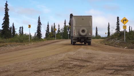 Static-shot-of-a-large-off-road-truck-turning-down-a-quiet-dirt-road-in-Alaska,-USA,-during-the-daytime