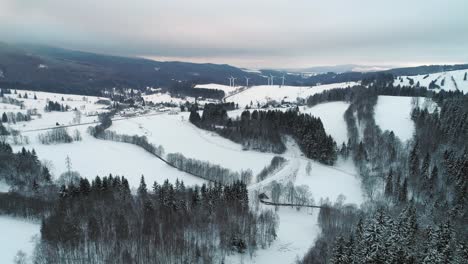 The-snow-white-covered-Ramzová-village-in-Czech-Republic-with-windmills-in-the-distance---aerial