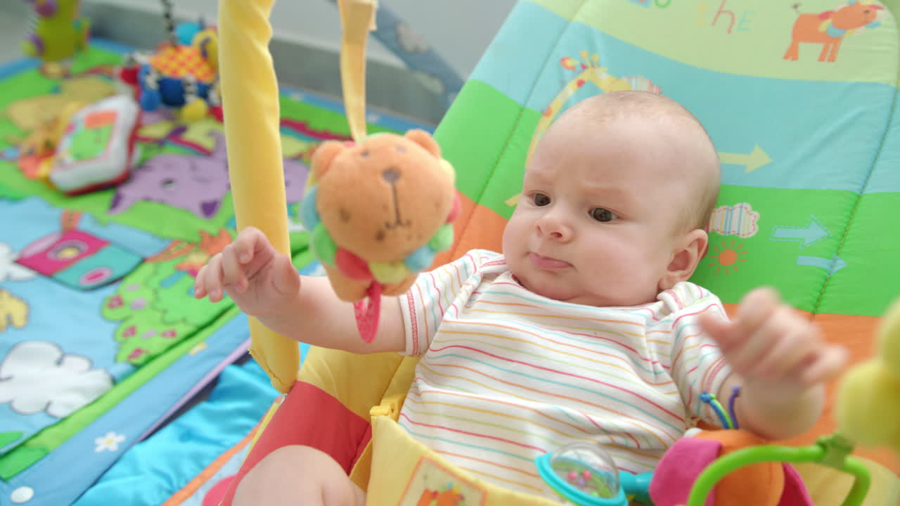 赤ちゃんの男の子はおもちゃのライオンを見ています. 可愛い子供がカラフルなラトルで遊んでいます