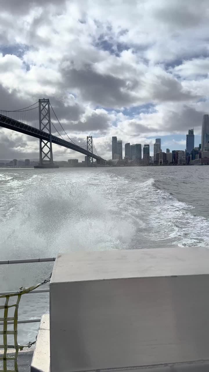 A stern view from a ferry showing the Bay Bridge and a distant San Francisco skyline, captured on an iPhone while crossing the bay. A perfect blend of urban and maritime scenery.
