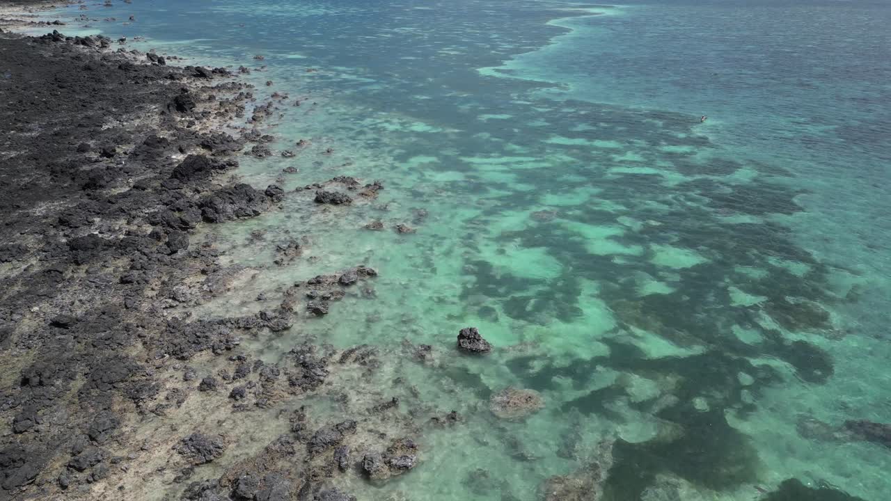 Aerial view of rocky volcanic coastline meeting clear turquoise ocean waters