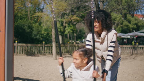child swinging with mom help in playground. family have fun.