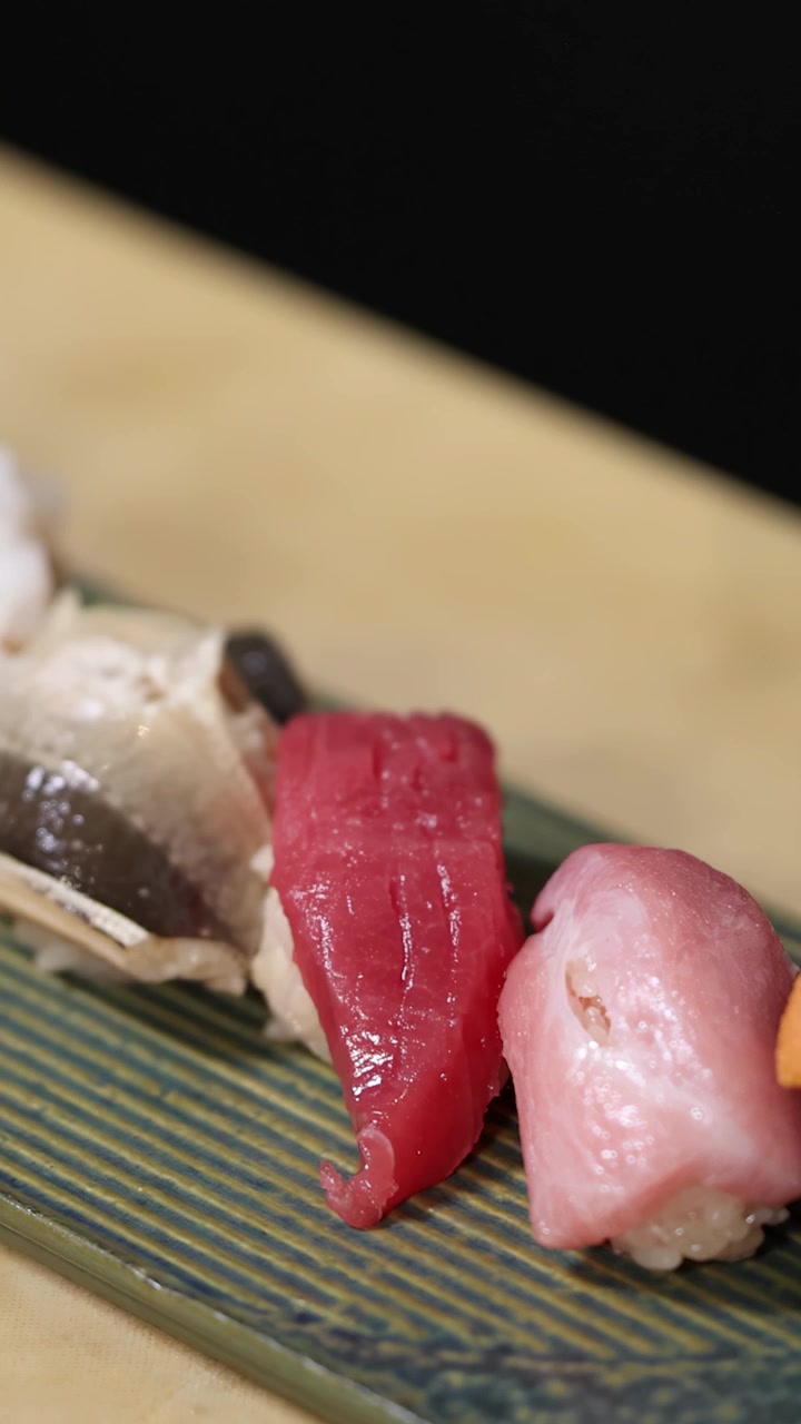 Inquadratura ravvicinata in movimento di sushi nigiri e gunkan premium disposti su un piatto di ceramica verde.