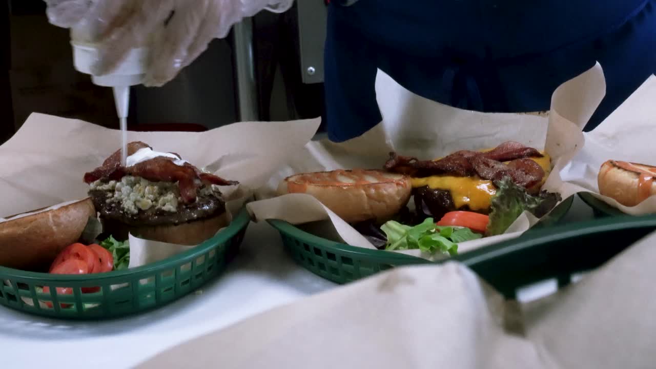 Cook preparing gourmet cheeseburgers with toppings and sauce in restaurant